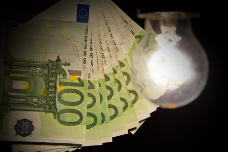 Hanging light bulb dangle on a wire illuminating bank notesの写真素材