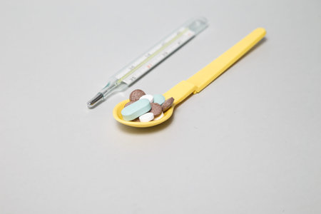 Spoon with pills and thermometer on table