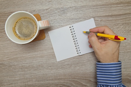 Male hand writing plans in notebook while as he drinks coffeeの写真素材