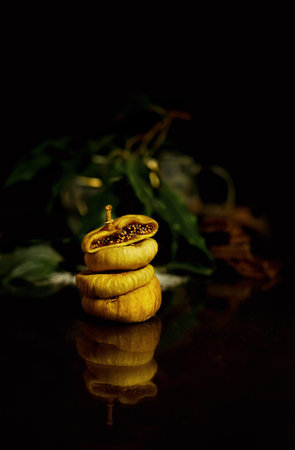 Pyramid of dried figs on a black table. The top figs are cut in half. Black background with live leaves.の写真素材