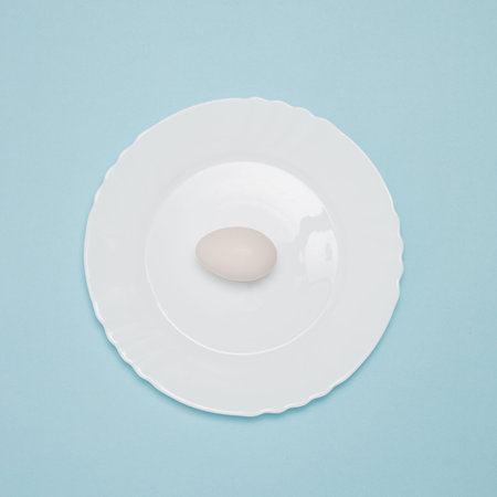 White plate and egg on pastel blue background. Minimal layout composition. Flat lay arrangement.