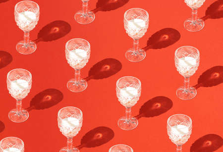 Pattern made of vine glasses fill with white milk fluid and sharp shadow on pastel red background. Minimal celebration concept. Trendy social mockup or wallpaper.の写真素材