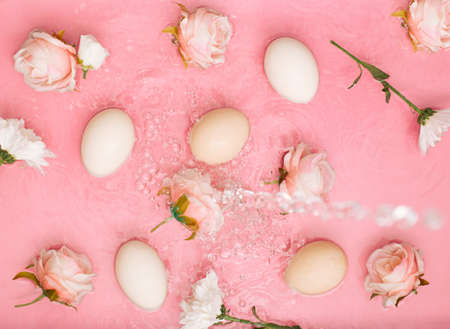 Easter scene with rose flowers and eggs in water with bubbles. Minimal natural pastel pink background.の写真素材