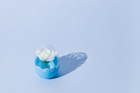 Creative composition done with white spring blossom inside the fashionable blue plastic egg on violet background. Minimal easter, spring mockup. Contemporary style. Natural sunlight lighting and sharp shadows.の写真素材