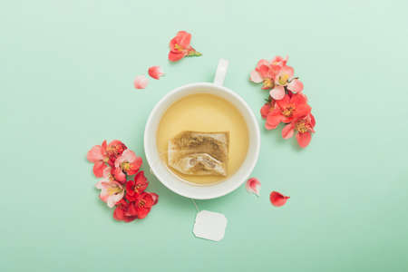 White ceramic cup with tea and red flowers on a pastel green background. Flower tea concept. Tea bag. Top viewの写真素材