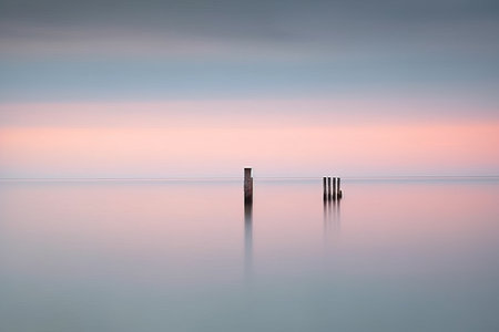 Two wooden poles in the sea at sunrise. Long exposure shot.の素材