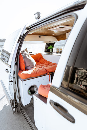 Beautiful bright natural light entering and illuminating an old self converted minivan campervan for van life. The vanlife recreational vehicle has orange seat cushions, stained roof, and van plant.の写真素材