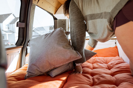 Young 30s caucasian woman with dark hair making the bed in a self converted minivan campervan for van life with lovely light coming in through the windows.の写真素材