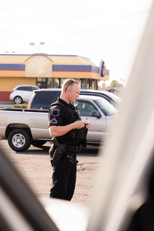 White male caucasian police officer cop trooper standing on street with black uniform and gun on hip...