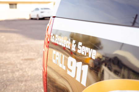 Horizontal image of back end of a police car vehicle reading Protect and serve call 911