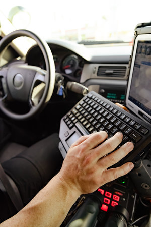 White male police officer hand and fingers typing on keyboard in cop vehicle searching for information to better help make informed decision to pull someone over or not.の写真素材