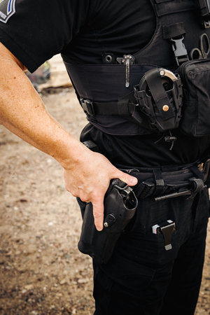 Vertical image of white male caucasian police officer reaching down and places hand on his weapon hand gun that is still in its holster on hip. Close up shot. No head.の写真素材