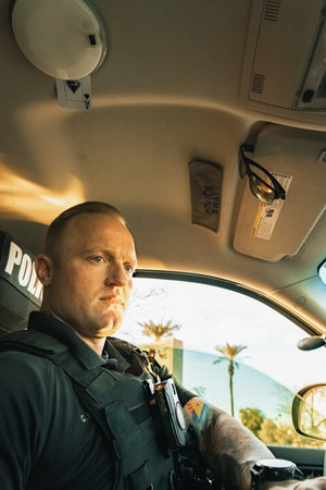 Vertical image low angle shot of of white male caucasian police officer sitting inside a cop vehicle...
