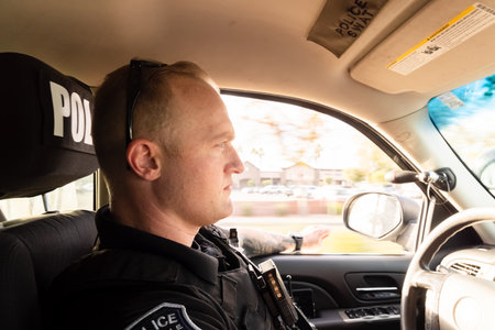 Horizontal image of white male caucasian police officer driving vehicle in city investigating possible situations in city on a warm afternoon with motion blur in background. Patrolling daytime.の写真素材