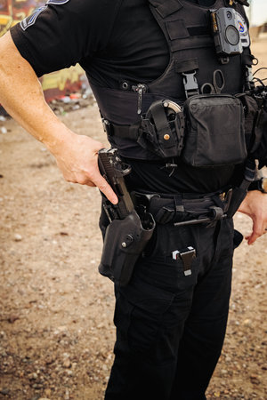 Vertical image of white male caucasian police officer reaching down and places hand on his weapon hand gun and pulls gun out of holster on hip. Close up shot. No head.の写真素材