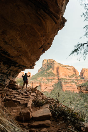 Solo female hiker on ledge with arms up to signify strength and achievement above Sedonaの写真素材