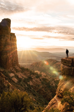Sun flare and young man at dramatic cliff at sunset at Cathedral Rock Sedonaの写真素材