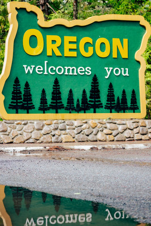 Closeup image of Oregon Welcomes You Sign on US-199 with reflection in puddle.の写真素材