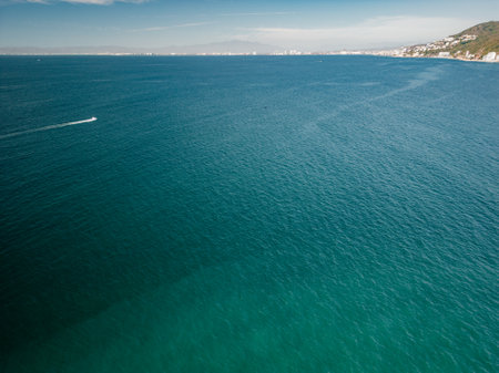 Wide expansive views of turquoise ocean below and Puerto Vallarta in the distance and boat driving.の写真素材