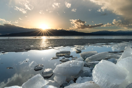 Ice stacks in vertical image at Vineyard Beach on Utah Lake in Utah at sunset with sun star in February 2025.の写真素材