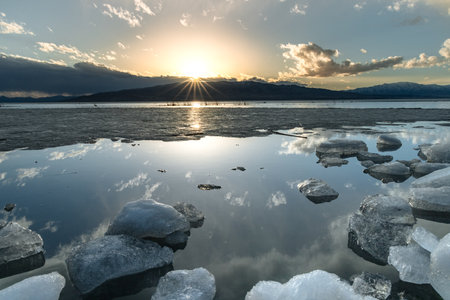 Ice stacks in horizontal image at Vineyard Beach on Utah Lake in Utah at sunset with sun star in February 2025.の写真素材
