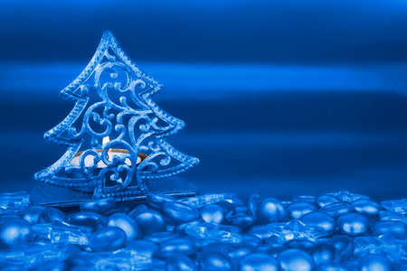 Christmas tree shaped tea light holder with blue clear glass stars and pebbles in foreground,の写真素材