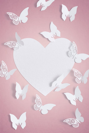 White butterfly Wedding Place Cards surrounding a love heart shaped blank textured paper for copy spaceの写真素材