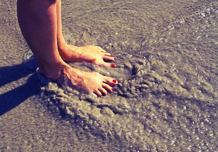 girls feet on the beach with the ocean ripplesの写真素材