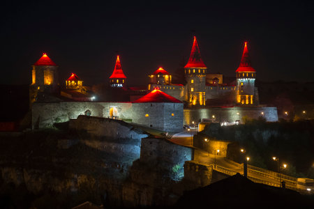Night shot of Kamianets-Podilskyi castle in Western Ukraine. The castle is brightly lit with red and yellow lighting.のeditorial素材