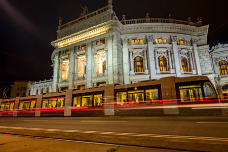 Static low angle night shot of tram arriving at stop in front of Burgtheater in Viennaのeditorial素材