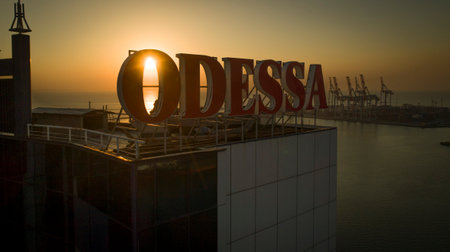 Sun rises behind large Odessa sign on top of the Odessa Hotel, Ukraine. The Black Sea and port are in the backgroundのeditorial素材