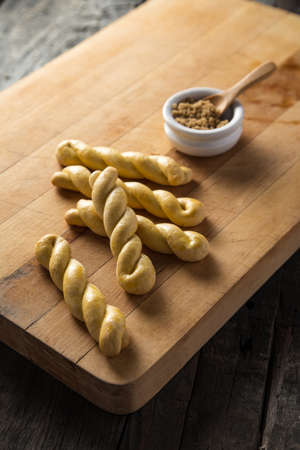 A breakfast spread of baked bread stick twists with a bowl of brown sugar placed on a black wooden...