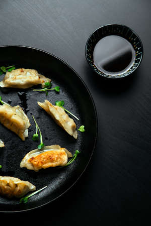 Traditional Japanese gyoza pot stickers cooked in a cast iron skillet with oil and green sprouts and placed on top of a modern black wood table.の写真素材