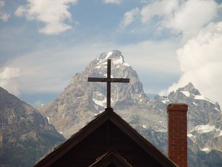 A cross is framed by mountains and blue skies.の写真素材