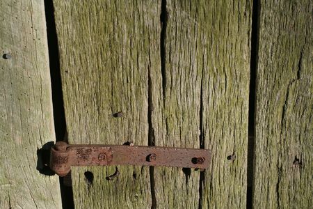 A very old and rusty hinge on a weathered wood door. 
