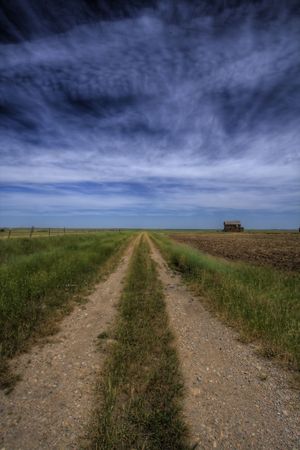 An old dirt road stretching far into the prairie with an abandoned home in the distance.  This is an HDR image.の写真素材