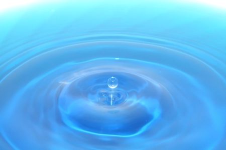 A water drop rising from a pool of water with ripples.の写真素材
