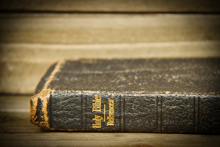 A Bible resting on its side on a wooden table with only the spine in focus with a slight vignette.の写真素材