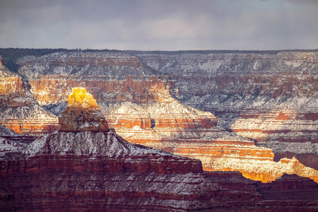 A winter evening in the Grand Canyon with snow in the high elevation and dramatic sunlight and shadows being cast into the canyon.の写真素材