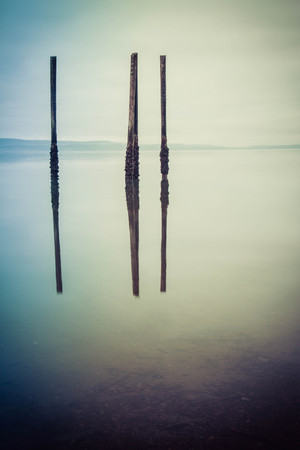 A gloomy image of the calm ocean with wood pilings standing free and reflecting in the water.の写真素材