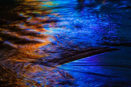 Warm and cool colors mixing and reflecting on the surface of water with small waves and ripples.の写真素材