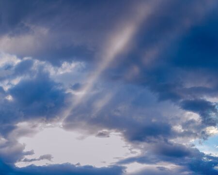 Sunbeams radiating out under colorful clouds during a sunset.の写真素材