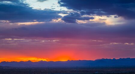Panorama of colorful clouds at sunset over an urban environment with mountains in the distance