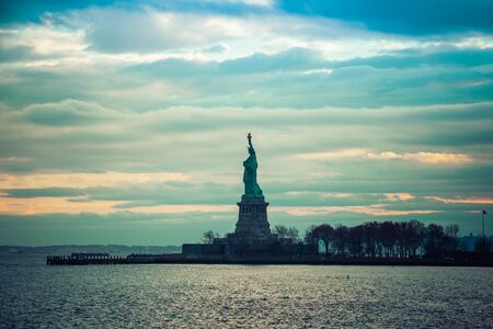 The Statute of Liberty standing in New York harbor during sunset.の写真素材