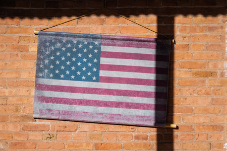 An old American flag on the side of a brick wall in sunlight.の写真素材