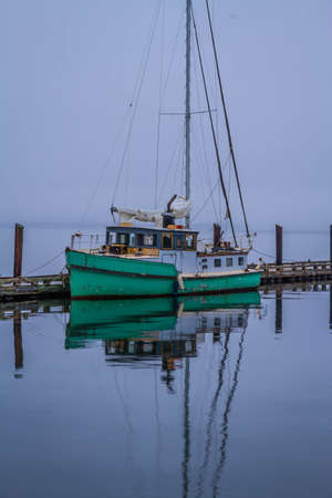 A 1945 converted KHE Army Boat moored at a pier on a cloudy morning with calm waters reflecting the boat.の写真素材