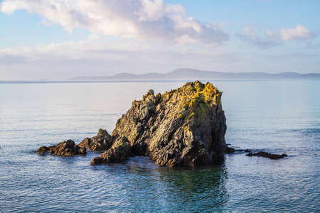 A single rock protruding from the surrounding blue ocean waters.の写真素材