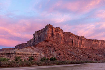 The brilliant colors of a sunrise reflecting on clouds over the top of a canyon wall with a river in the foreground in Utah.の写真素材