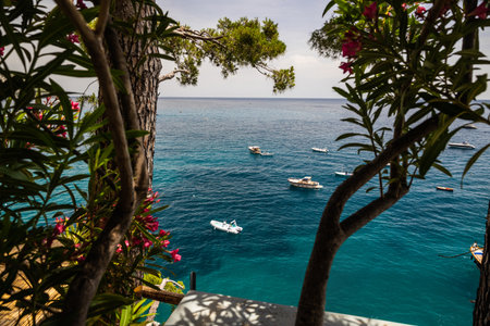 A view of boast floating on the blue water of the Mediterranean Sea through trees along the Amalfi Coast in Positano, Italy, Europe.の写真素材