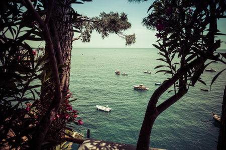 A view of boast floating on the blue water of the Mediterranean Sea through trees along the Amalfi Coast in Positano, Italy, Europe.の写真素材